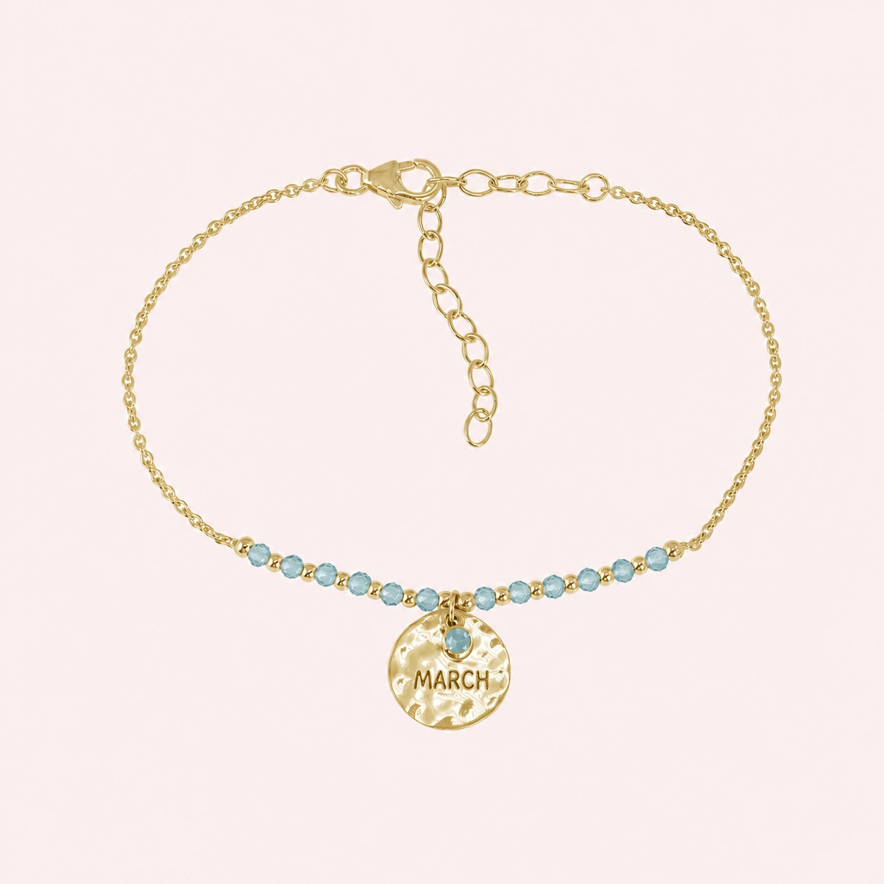 Birthstone_bracelet_in_gold_plated_silver_with_March_charm_and_aqua_marine_beads_on_fine_chain_on_solid_pink_background