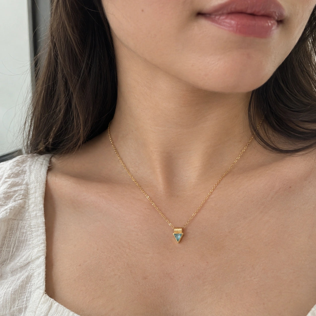 Aquamarine_necklace_in_gold_plated_silver_with_a_triangle_stone_in_front_angle_on_a_white_fabric_background