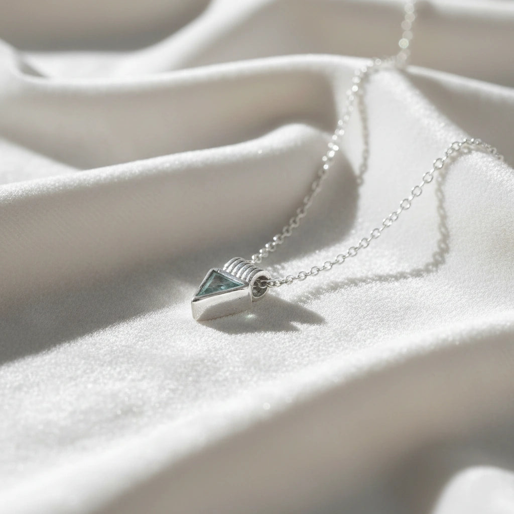 Aquamarine_necklace_in_sterling_silver_with_a_triangle_stone_in_slight_angle_on_a_white_fabric_background