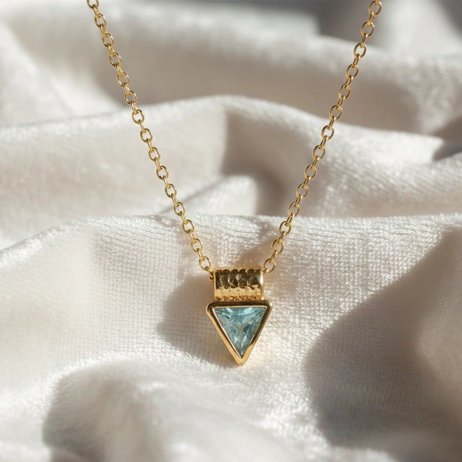 Aquamarine_necklace_in_gold_plated_silver_with_a_triangle_stone_in_front_angle_on_a_white_fabric_background