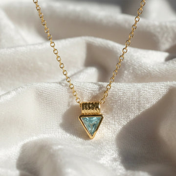 Aquamarine_necklace_in_gold_plated_silver_with_a_triangle_stone_in_front_angle_on_a_white_fabric_background