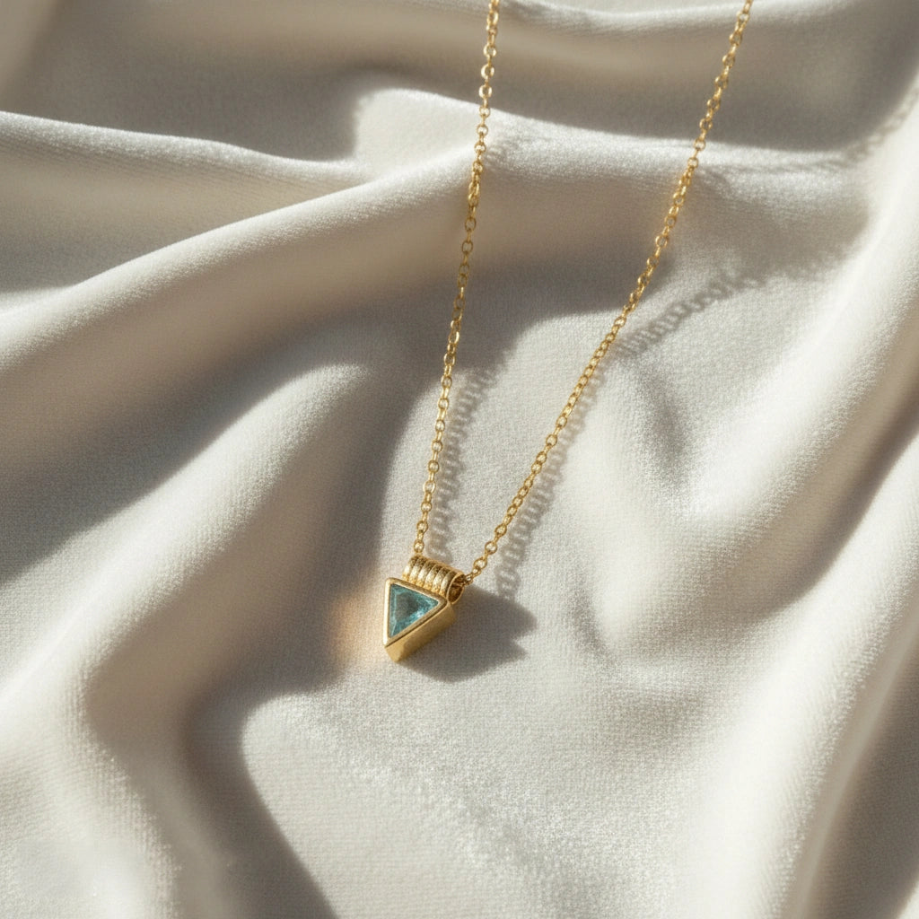 Aquamarine_necklace_in_gold_plated_silver_with_a_triangle_stone_in_slight_angle_on_a_white_fabric_background