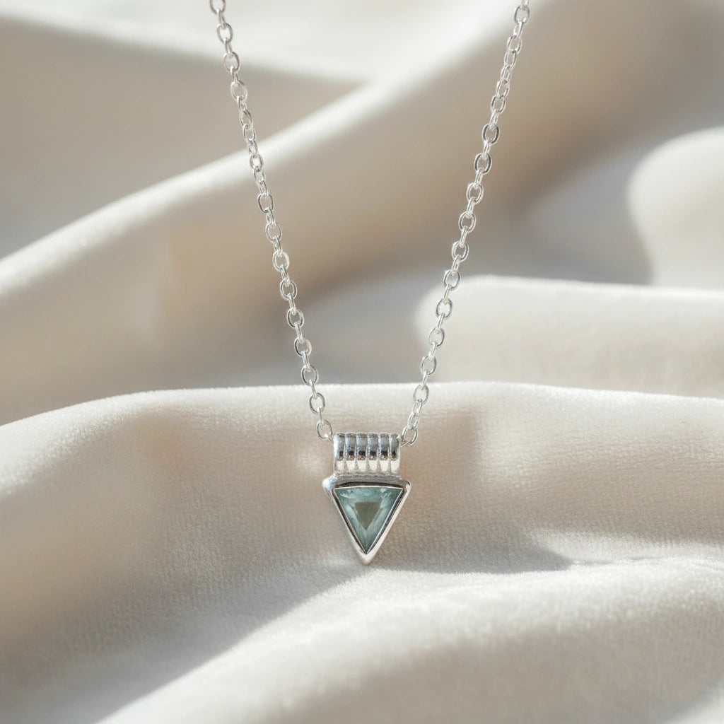 Aquamarine_necklace_in_sterling_silver_with_a_triangle_stone_in_front_angle_on_a_white_fabric_background