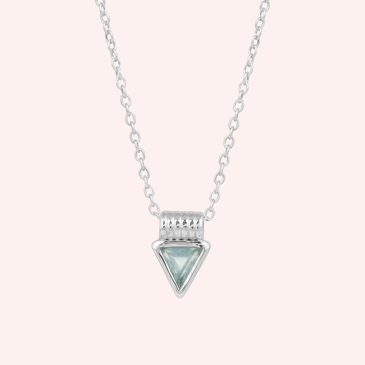 Aquamarine_necklace_in_sterling_silver_with_a_triangle_stone_in_front_angle_on_a_solid_pink_background