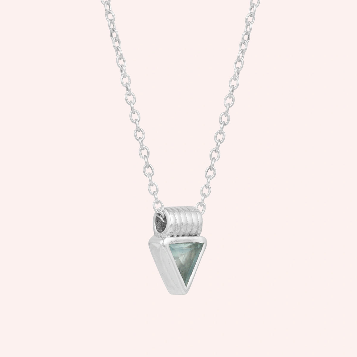 Aquamarine_necklace_in_sterling_silver_with_a_triangle_stone_in_slight_angle_on_a_solid_pink_background
