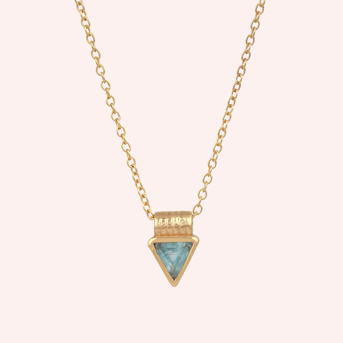 Aquamarine_necklace_in_gold_plated_silver_with_a_triangle_stone_in_front_angle_on_a_solid_pink_background