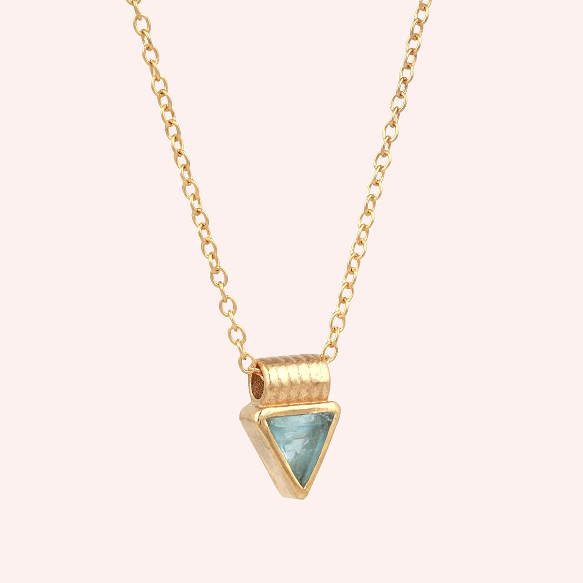 Aquamarine_necklace_in_gold_plated_silver_with_a_triangle_stone_in_slight_angle_on_a_solid_pink_background