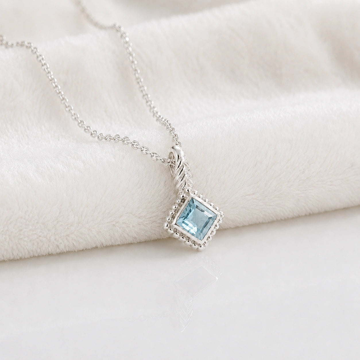 Birthstone_necklace_in_sterling_silver_with_square_cut_aquamarine_pendant_in_slighlty_angled_view_on_soft_white_fabric_background