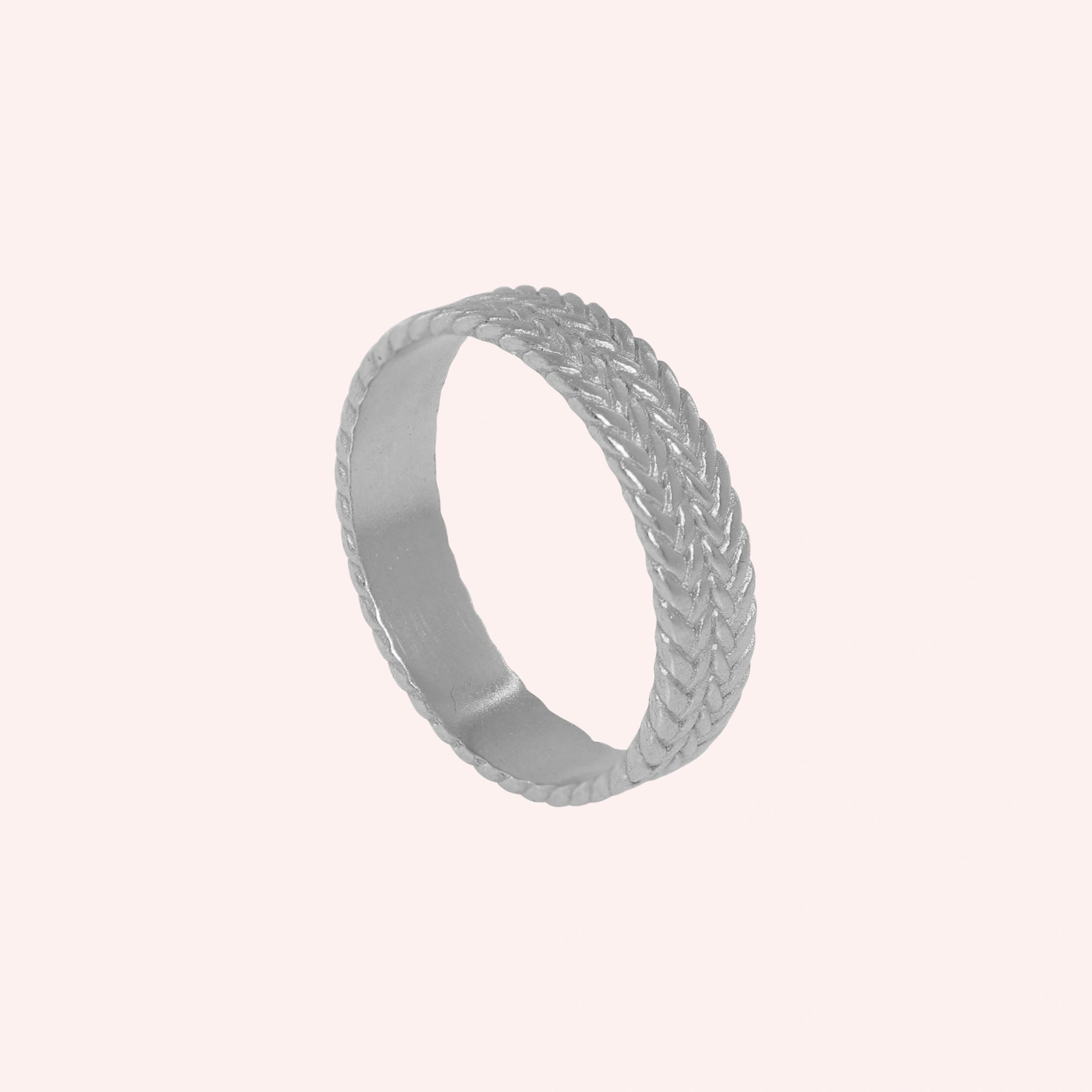 Band_ring_in_sterling_silver_with_braided_design_at_angle_view_on_solid_pink_background