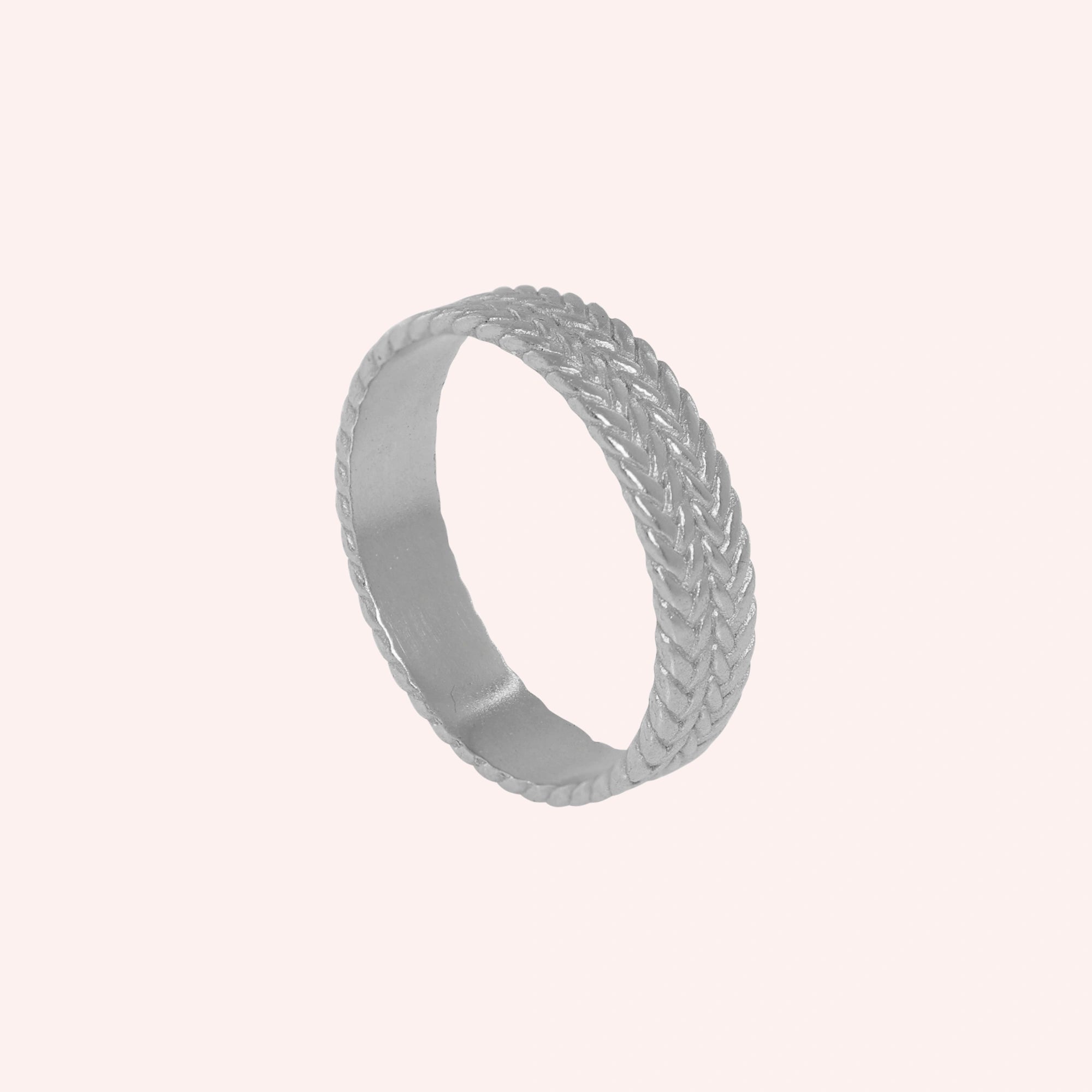 Band_ring_in_sterling_silver_with_braided_design_at_angle_view_on_solid_pink_background