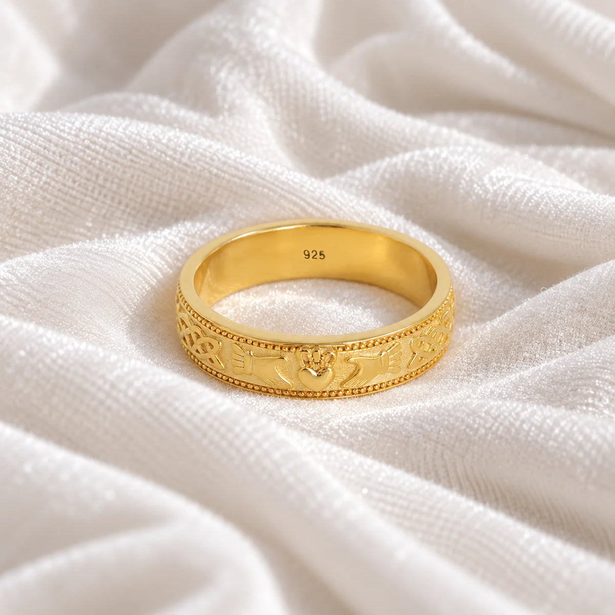 Band_ring_in_gold_plated_silver_with_claddagh_design_at_front_angle_view_on_soft_fabric_background