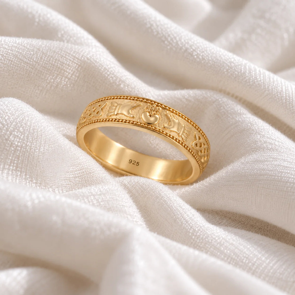 Band_ring_in_gold_plated_silver_with_claddagh_design_at_slight_angle_view_on_soft_fabric_background