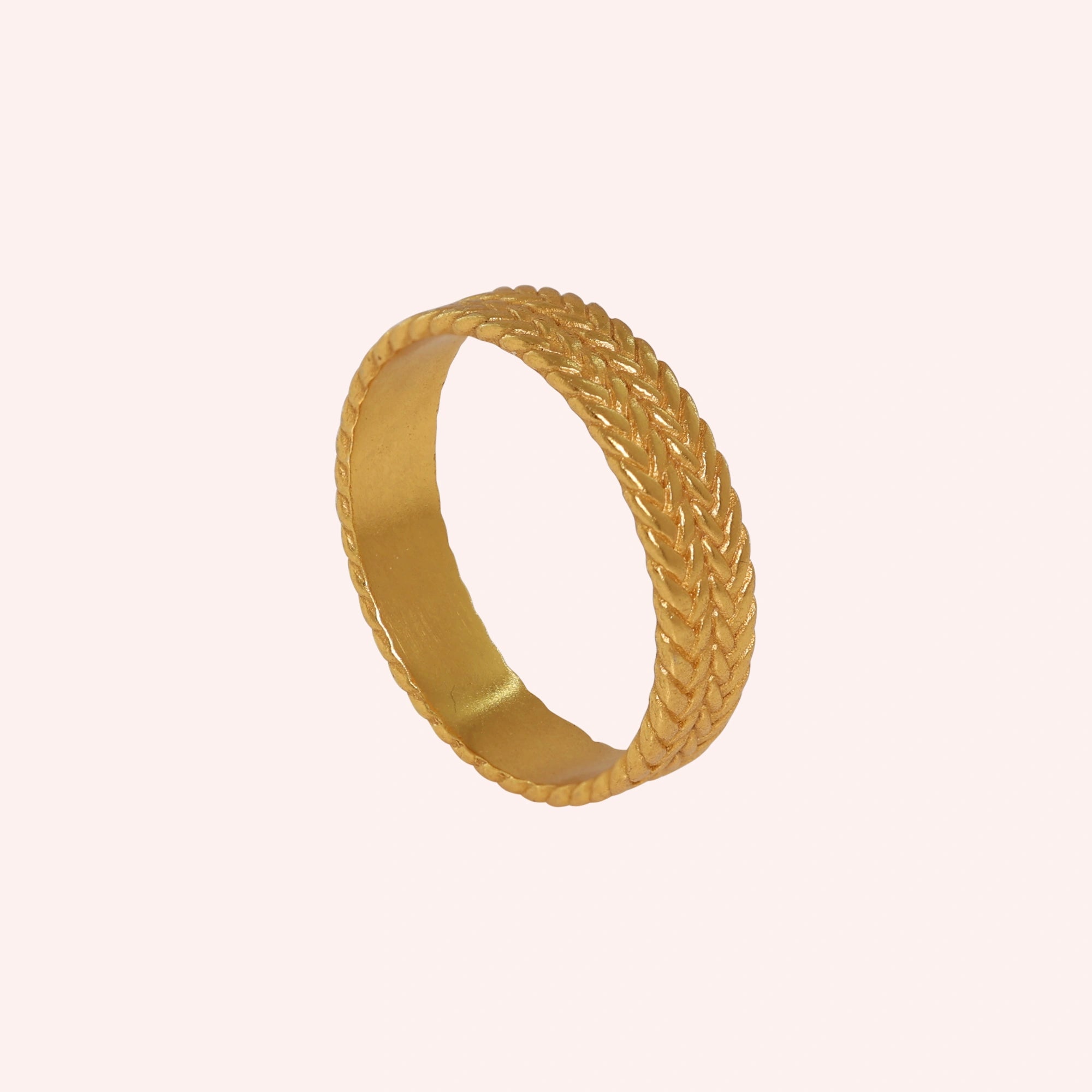 Band_ring_in_gold_plated_silver_with_braided_design_at_angle_view_on_solid_pink_background