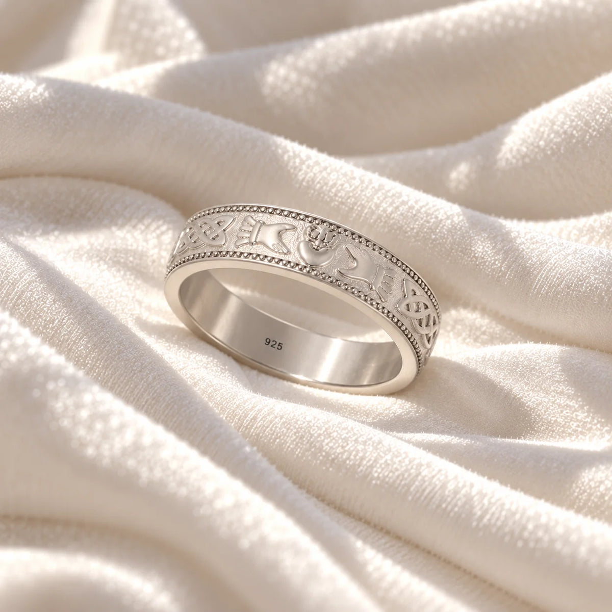 Band_ring_in_sterling_silver_with_claddagh_design_at_slight_angle_view_on_soft_fabric_background