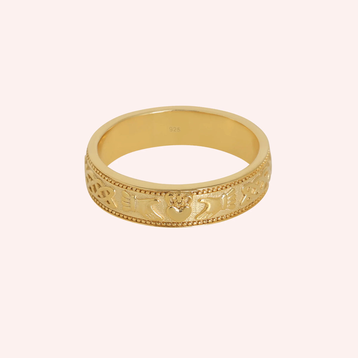Band_ring_in_gold_plated_silver_with_claddagh_design_at_front_angle_view_on_solid_pink_background