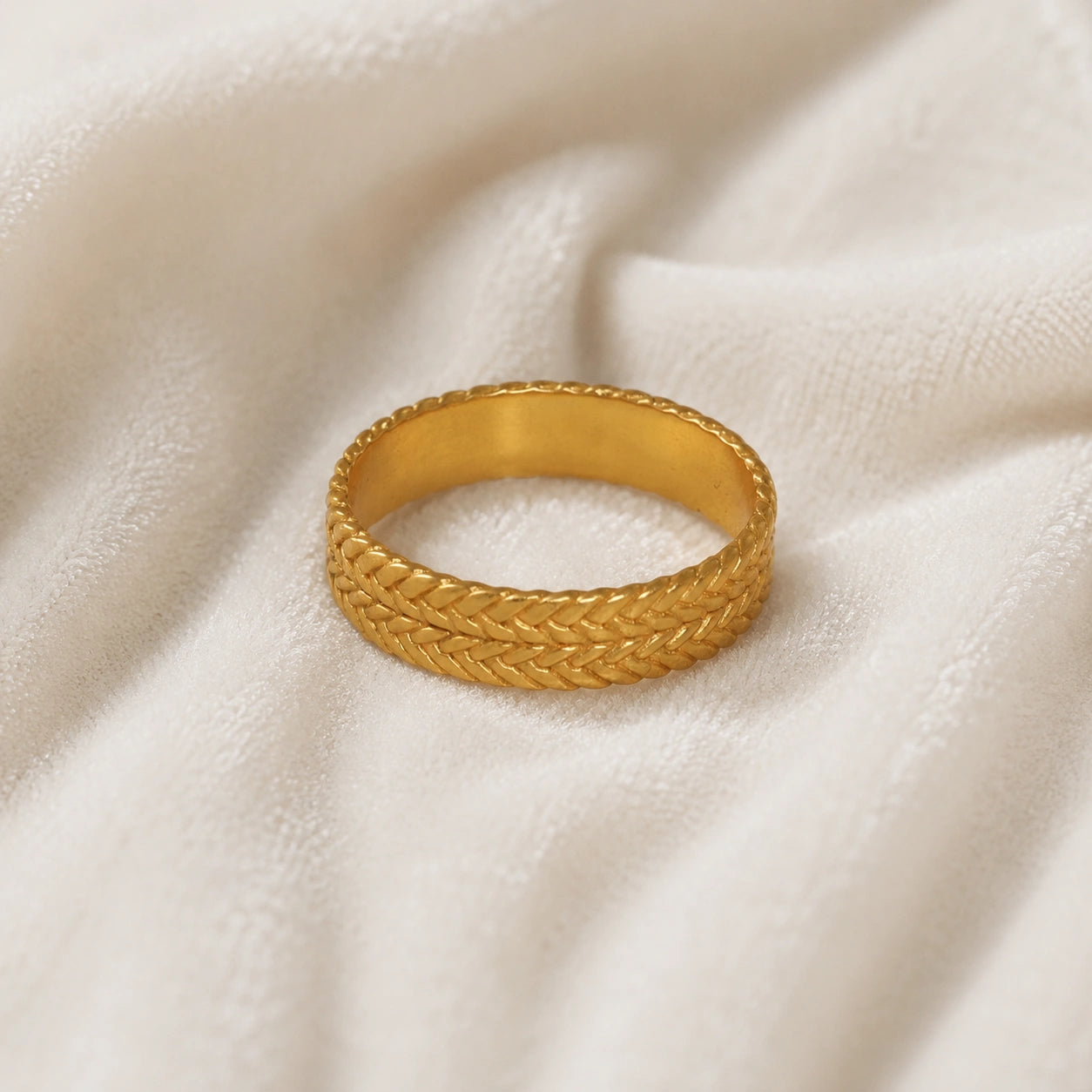 Band_ring_in_gold_plated_silver_with_braided_design_at_front_angle_on_soft_pink_background