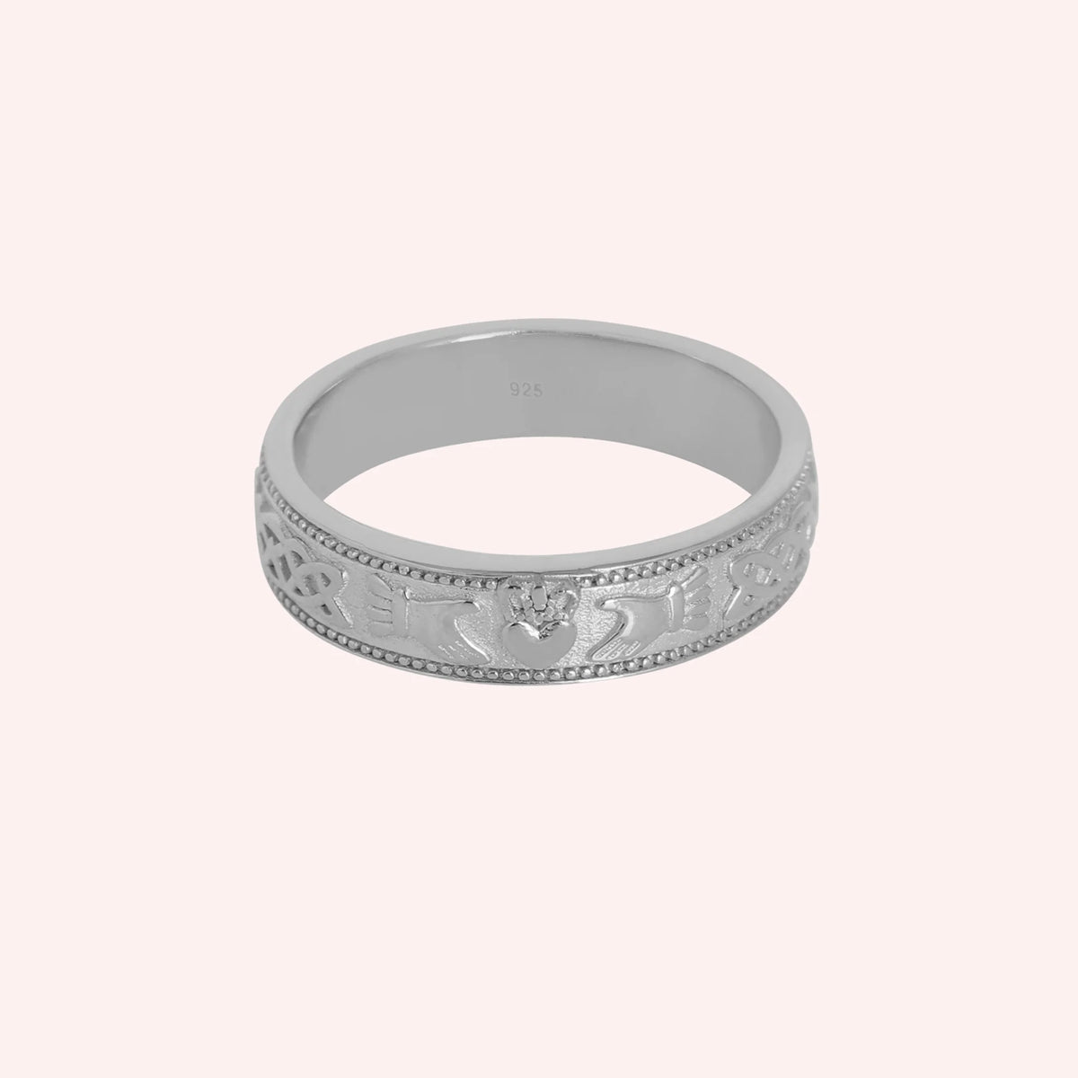 Band_ring_in_sterling_silver_with_claddagh_design_at_front_angle_view_on_solid_pink_background