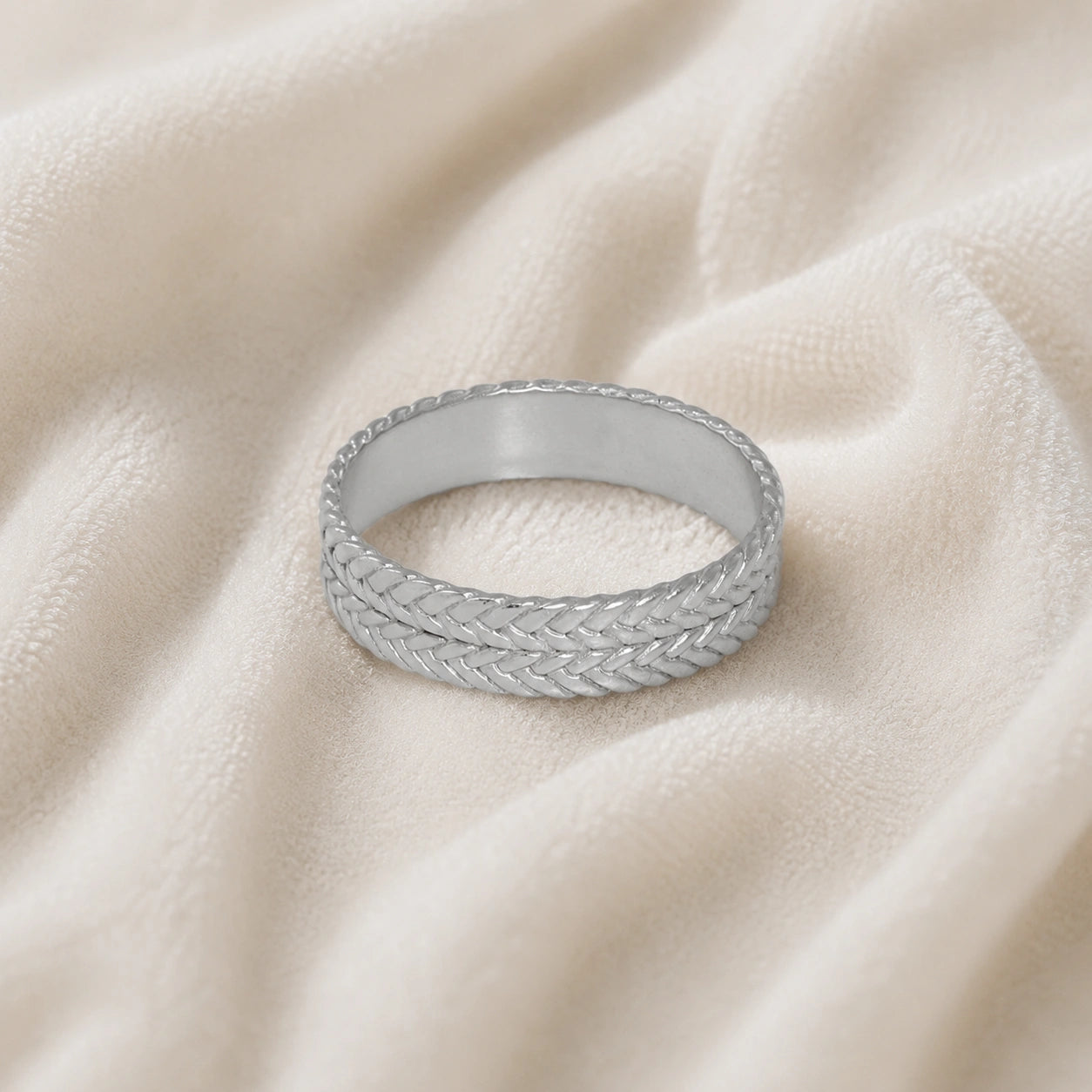 Band_ring_in_sterling_silver_with_braided_design_at_front_angle_on_soft_pink_background