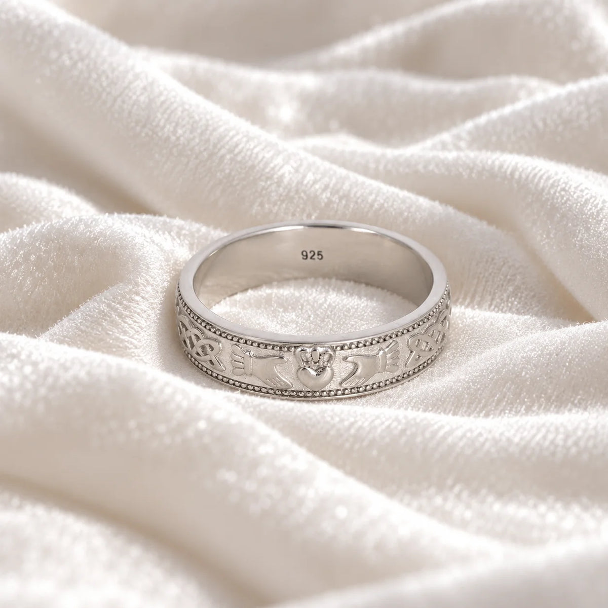 Band_ring_in_sterling_silver_with_claddagh_design_at_front_angle_view_on_soft_fabric_background