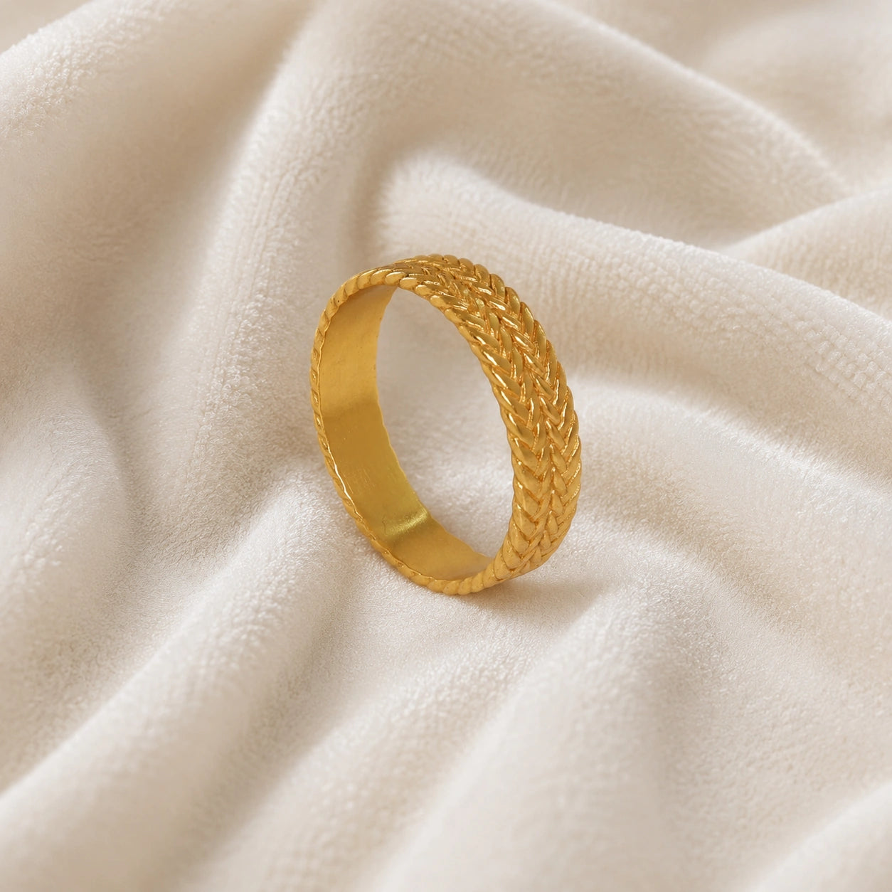Band_ring_in_gold_plated_silver_with_braided_design_at_angle_view_on_soft_fabric_background