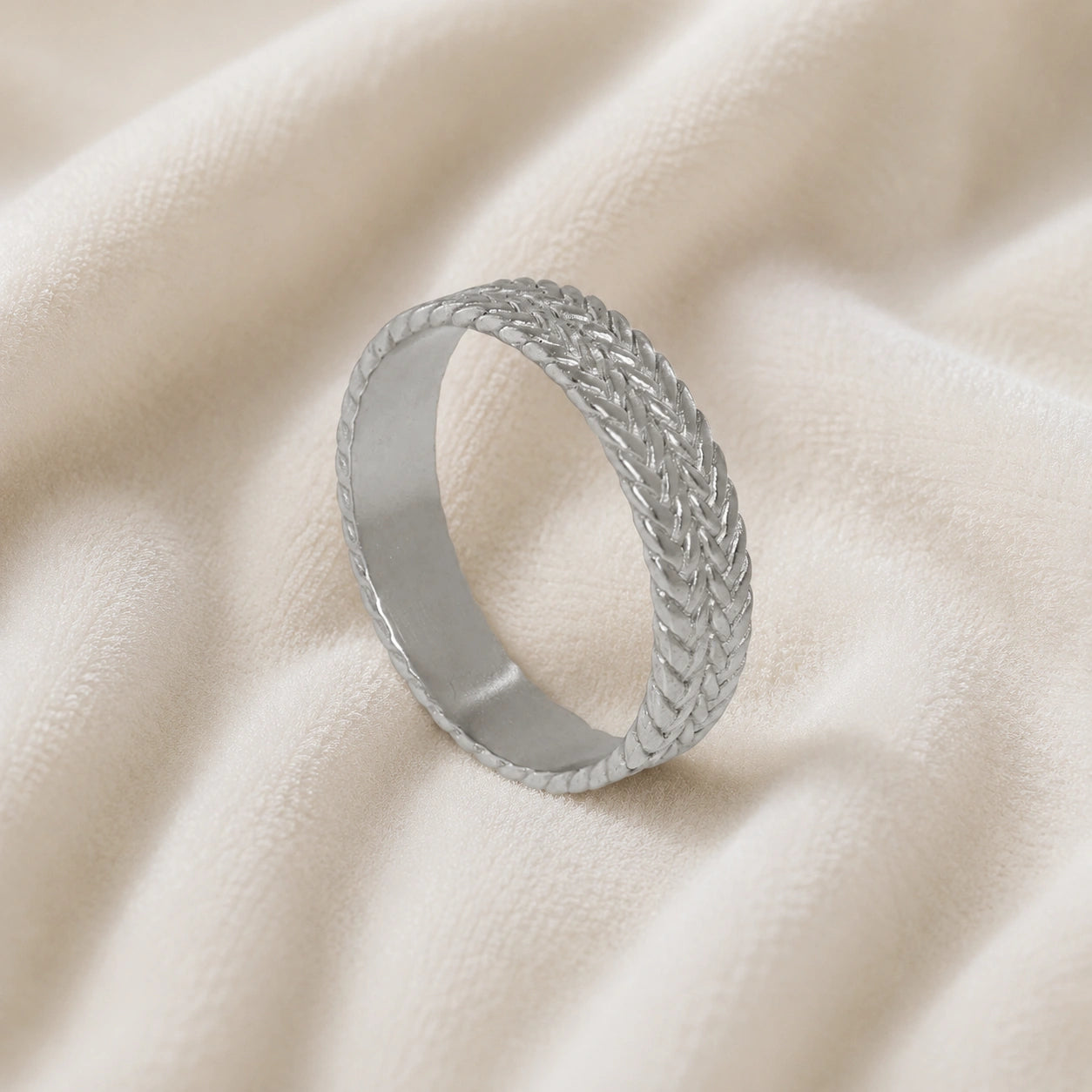 Band_ring_in_sterling_silver_with_braided_design_at_angle_view_on_soft_fabric_background
