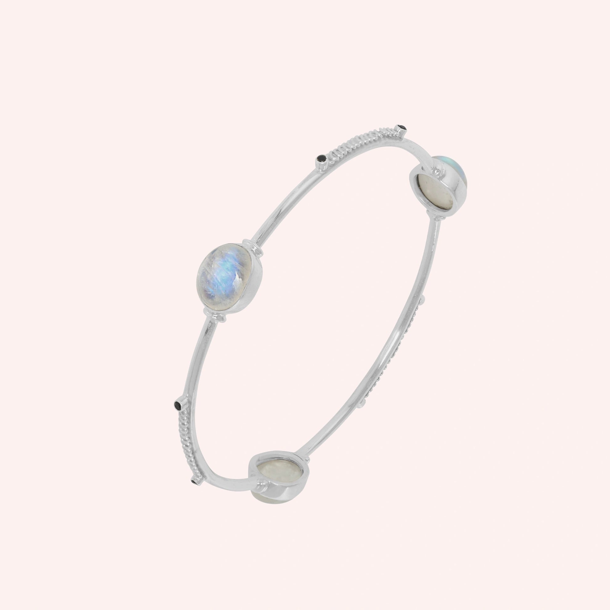 Bangle_bracelet_in_sterling_silver_with_oval_moonstones_and_black_onyx_stones_at_slight_angle_view_on_solid_pink_background