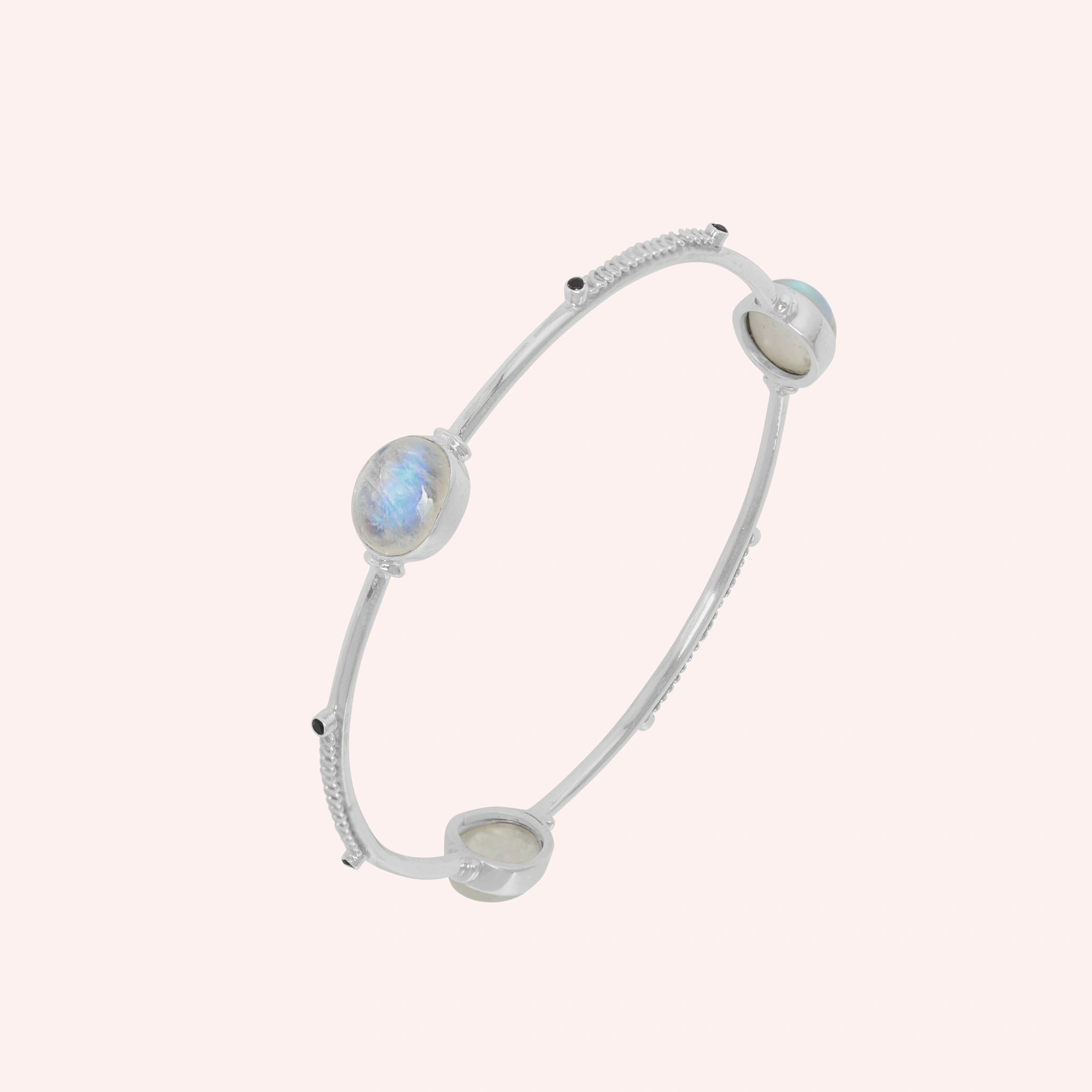 Bangle_bracelet_in_sterling_silver_with_oval_moonstones_and_black_onyx_stones_at_slight_angle_view_on_solid_pink_background