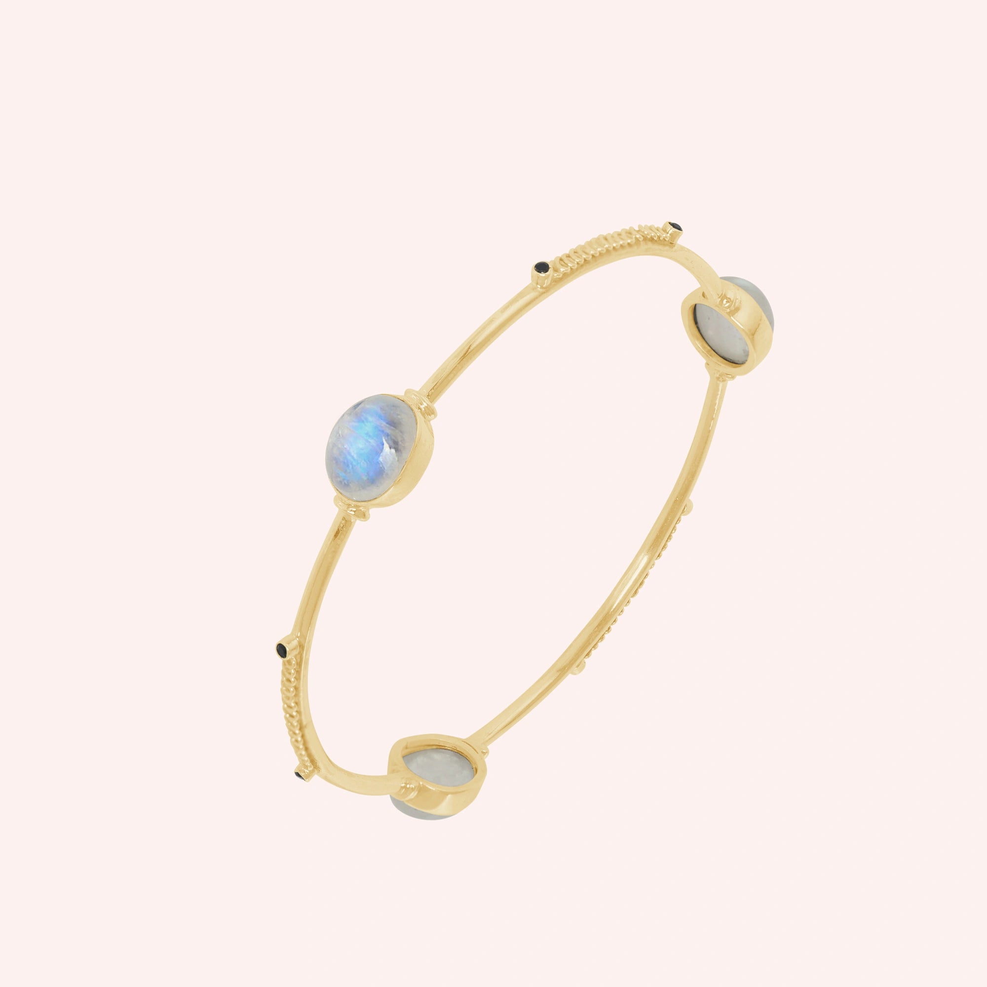 Bangle_bracelet_in_gold_plated_silver_with_oval_moonstones_and_black_onyx_stones_at_slight_angle_view_on_solid_pink_background