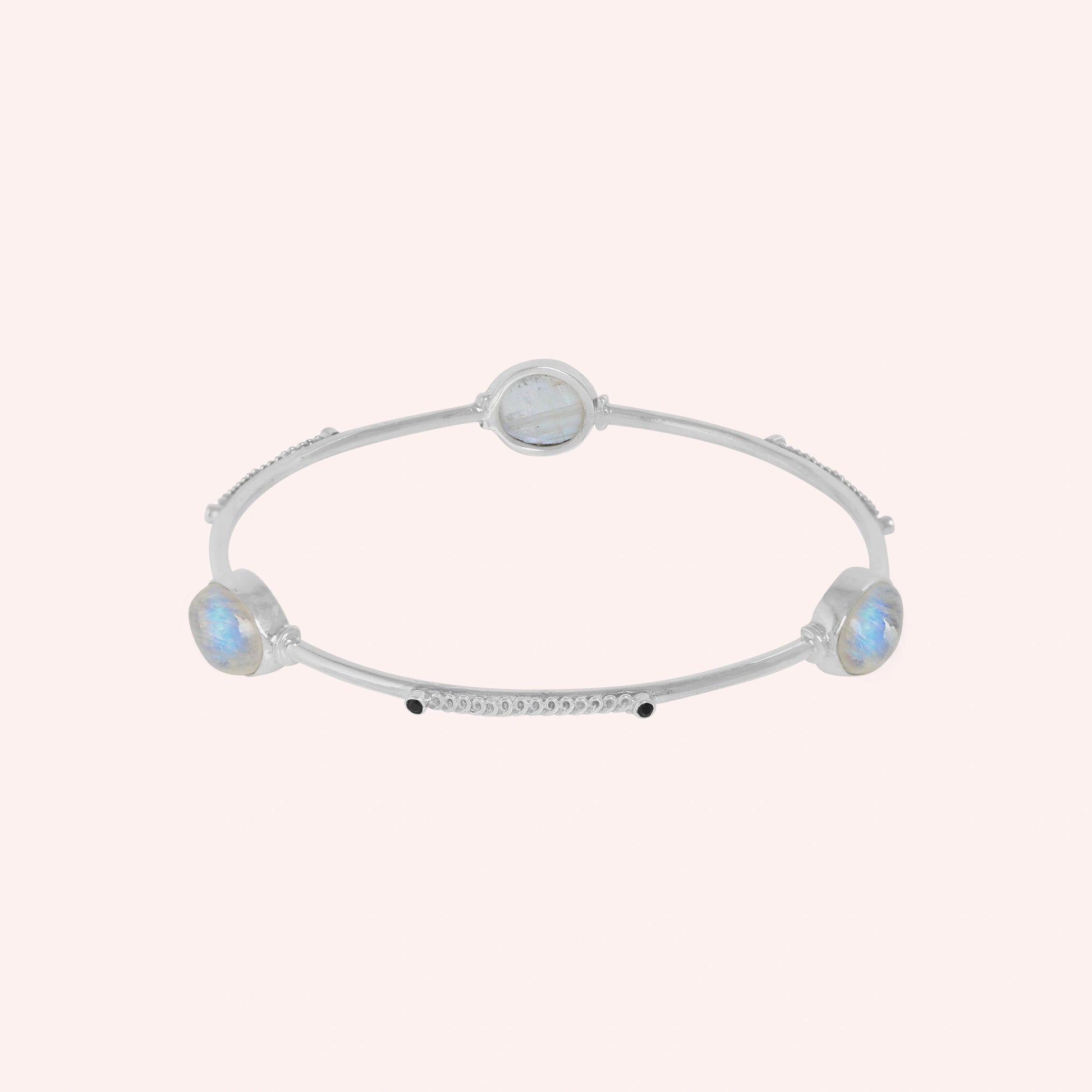 Bangle_bracelet_in_sterling_silver_with_oval_moonstones_and_black_onyx_stones_at_front_angle_view_on_solid_pink_background