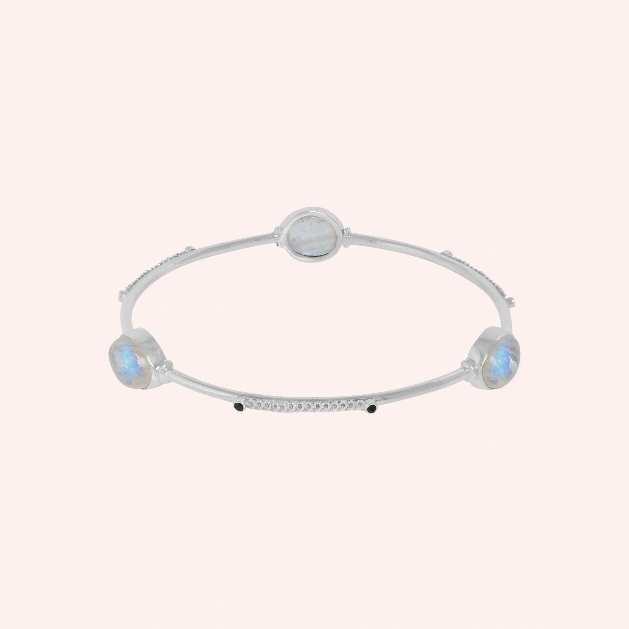 Bangle_bracelet_in_sterling_silver_with_oval_moonstones_and_black_onyx_stones_at_front_angle_view_on_solid_pink_background