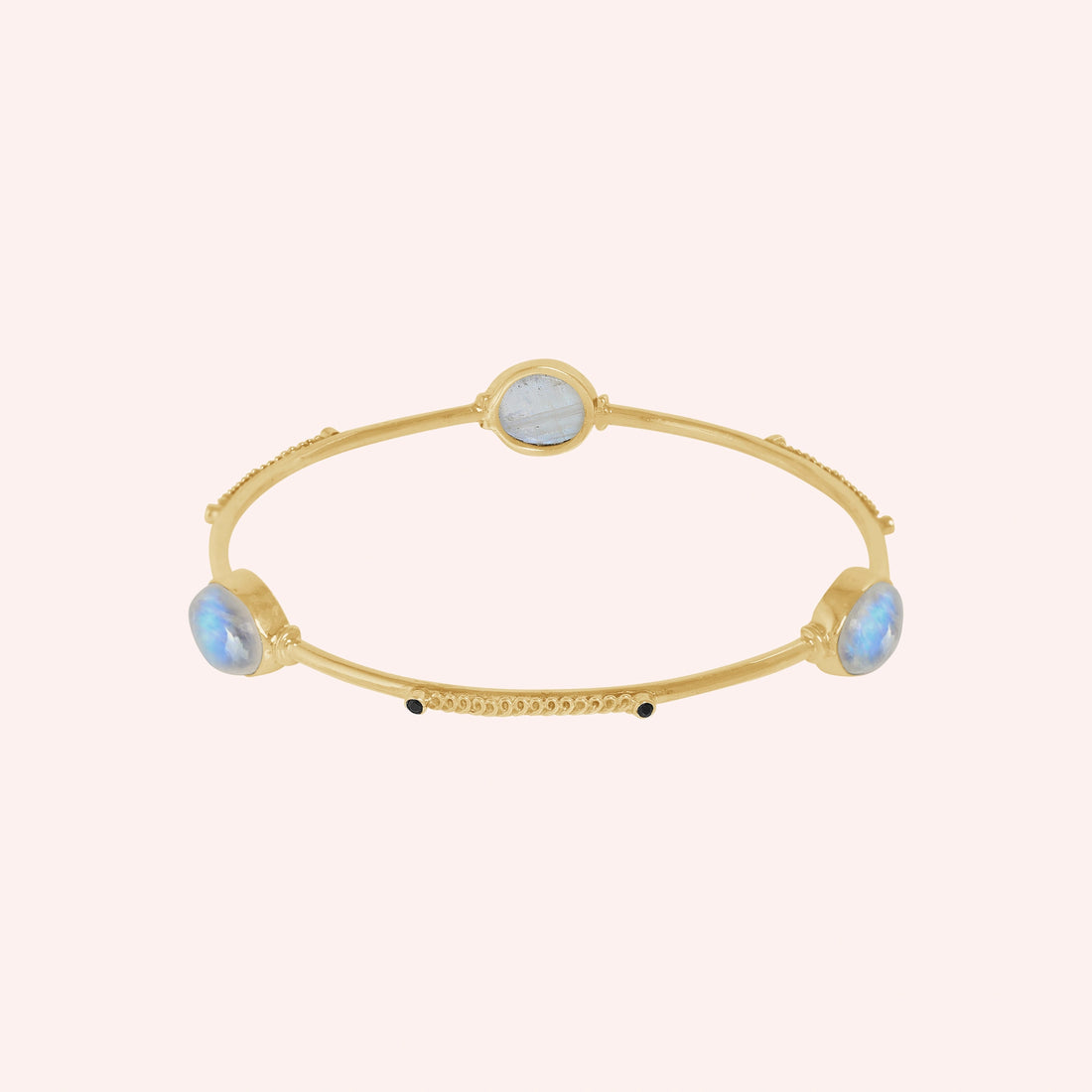 Bangle_bracelet_in_gold_plated_silver_with_oval_moonstones_and_black_onyx_stones_at_front_angle_view_on_solid_pink_background