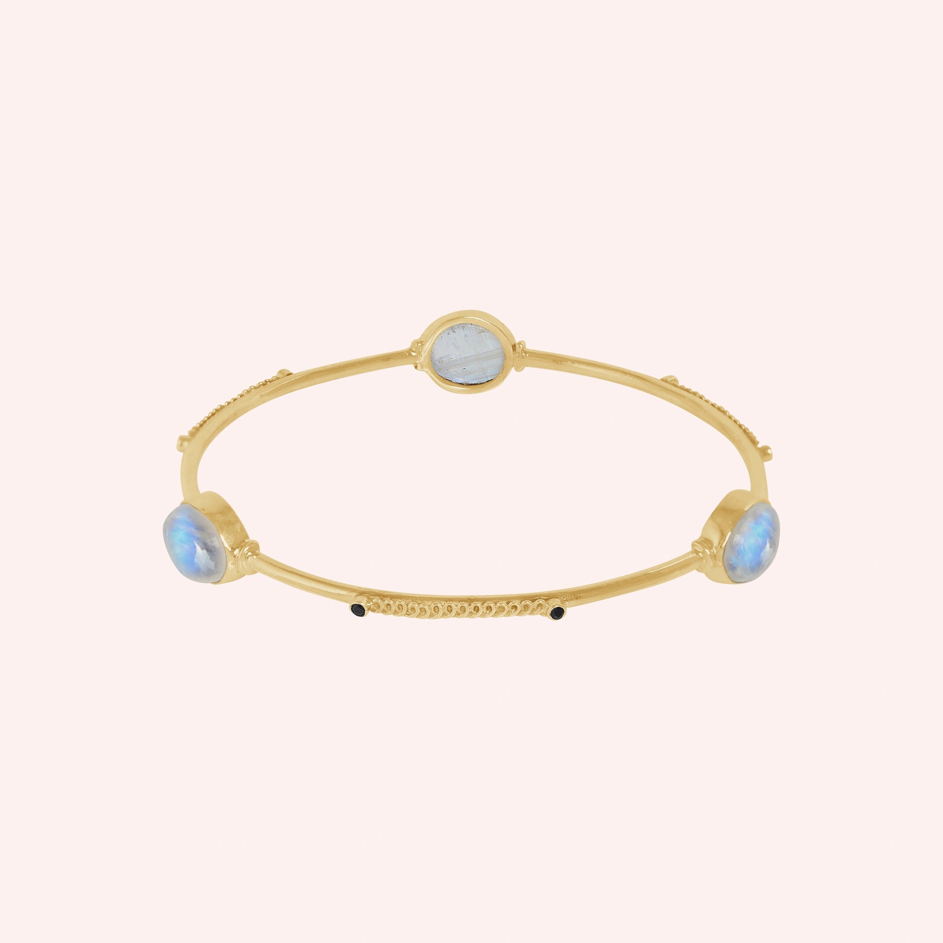 Bangle_bracelet_in_gold_plated_silver_with_oval_moonstones_and_black_onyx_stones_at_front_angle_view_on_solid_pink_background