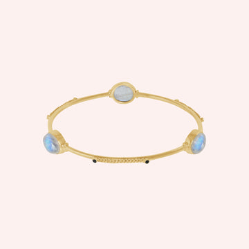 Bangle_bracelet_in_gold_plated_silver_with_oval_moonstones_and_black_onyx_stones_at_front_angle_view_on_solid_pink_background