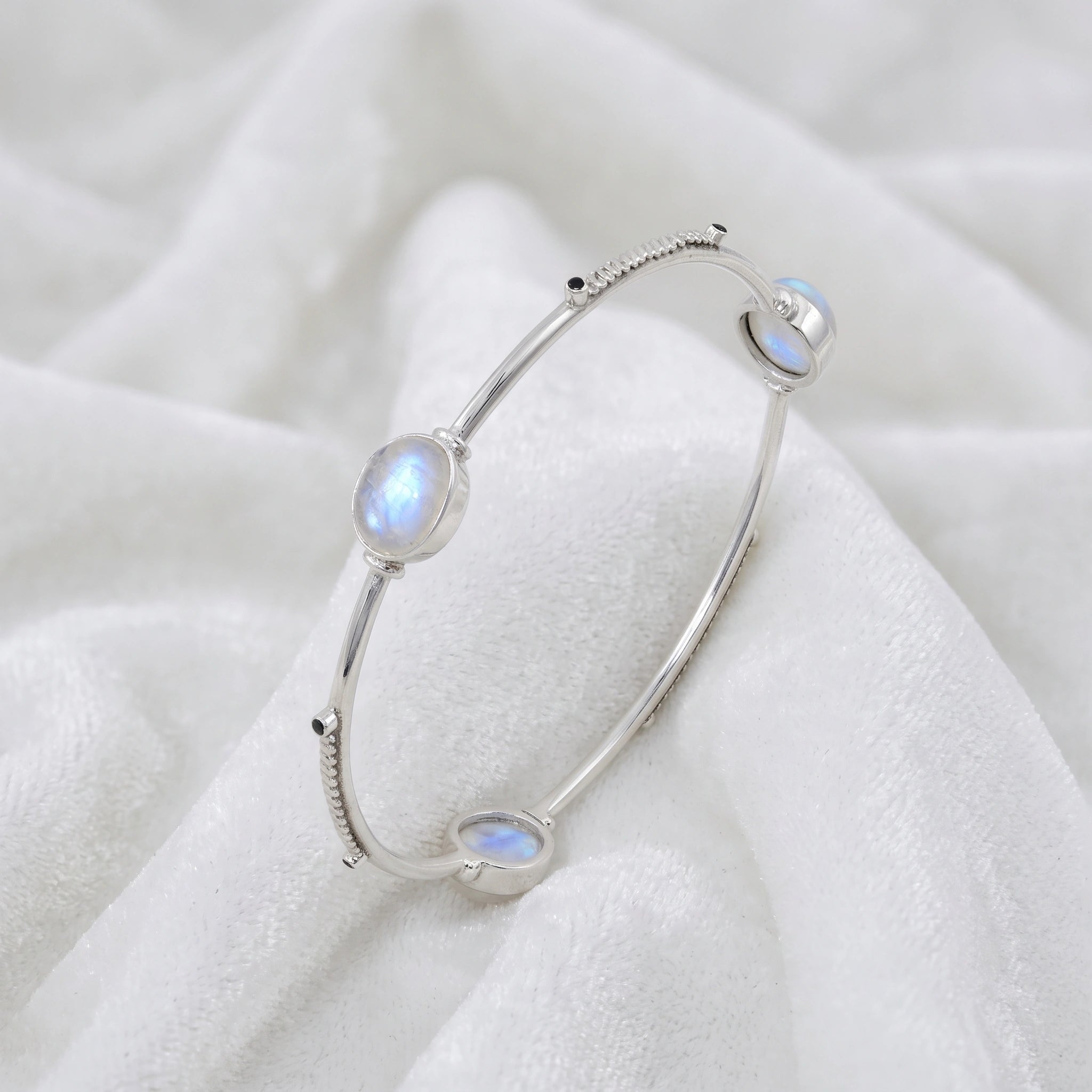 Bangle_bracelet_in_sterling_silver_with_oval_moonstones_and_black_onyx_stones_at_slight_angle_view_on_soft_fabric_background