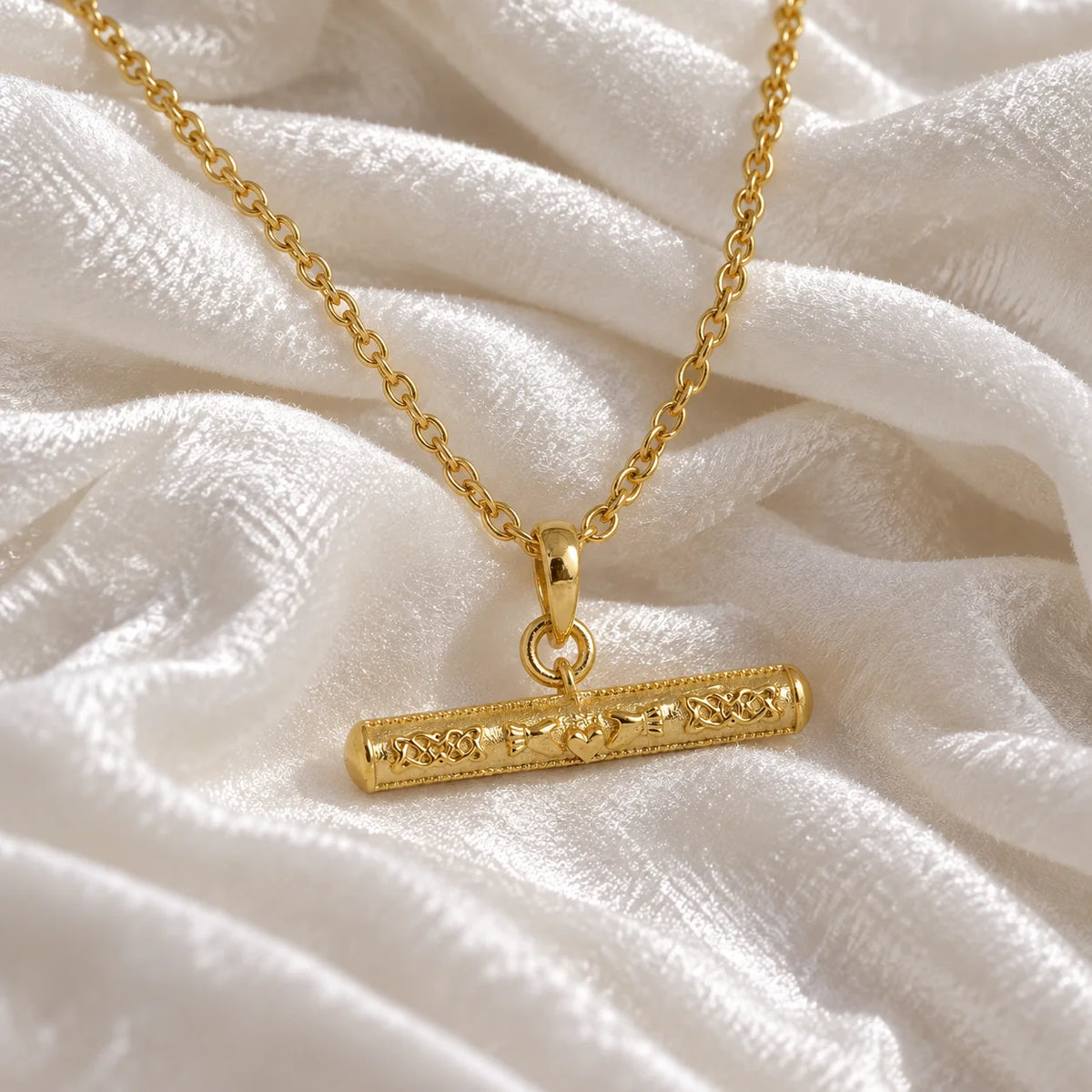 Bar_necklace_in_gold_plated_silver_with_claddagh_design_at_slight_angle_view_on_soft_fabric_background