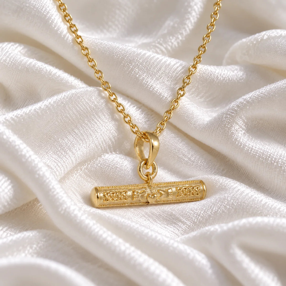 Bar_necklace_in_gold_plated_silver_with_claddagh_design_at_front_angle_view_on_soft_fabric_background
