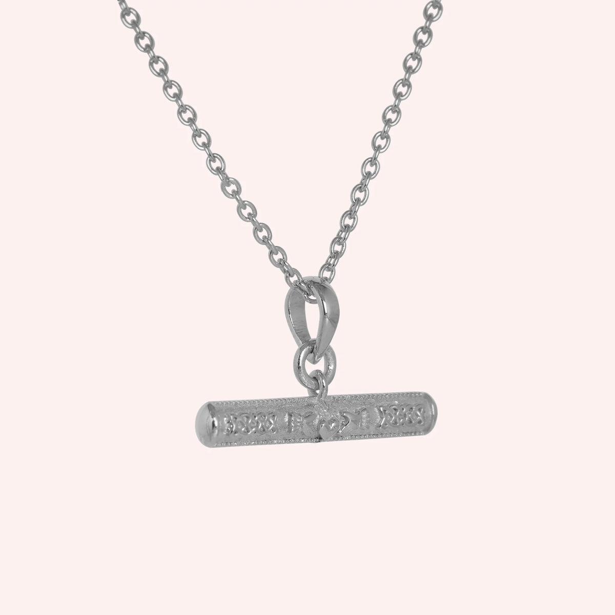Bar_necklace_in_sterling_silver_with_claddagh_design_at_slight_angle_view_on_solid_pink_background