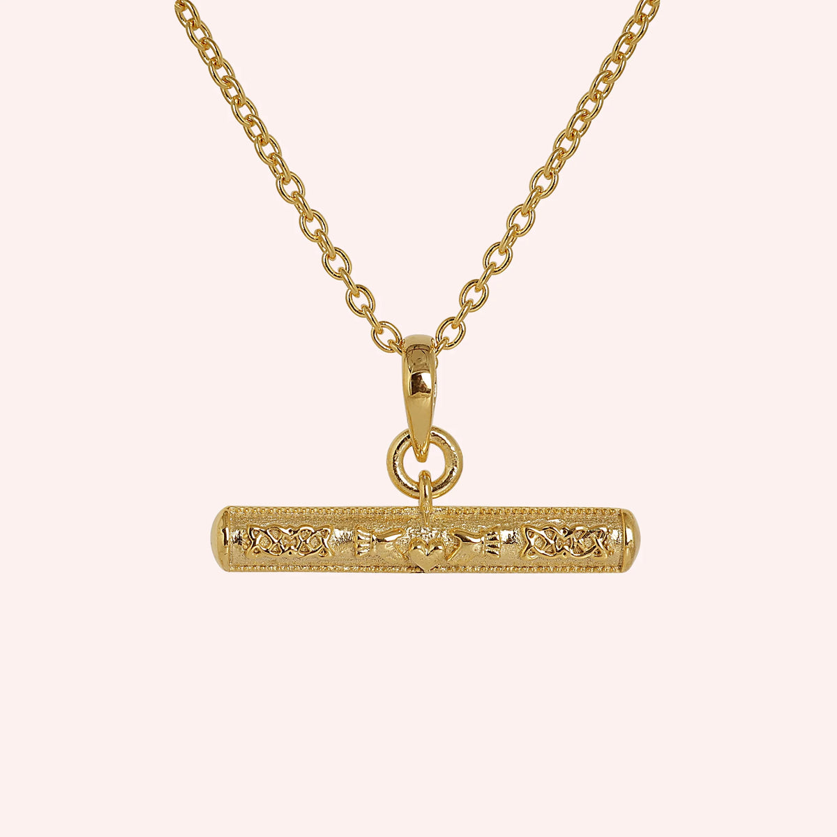 Bar_necklace_in_gold_plated_silver_with_claddagh_design_at_front_angle_view_on_solid_pink_background