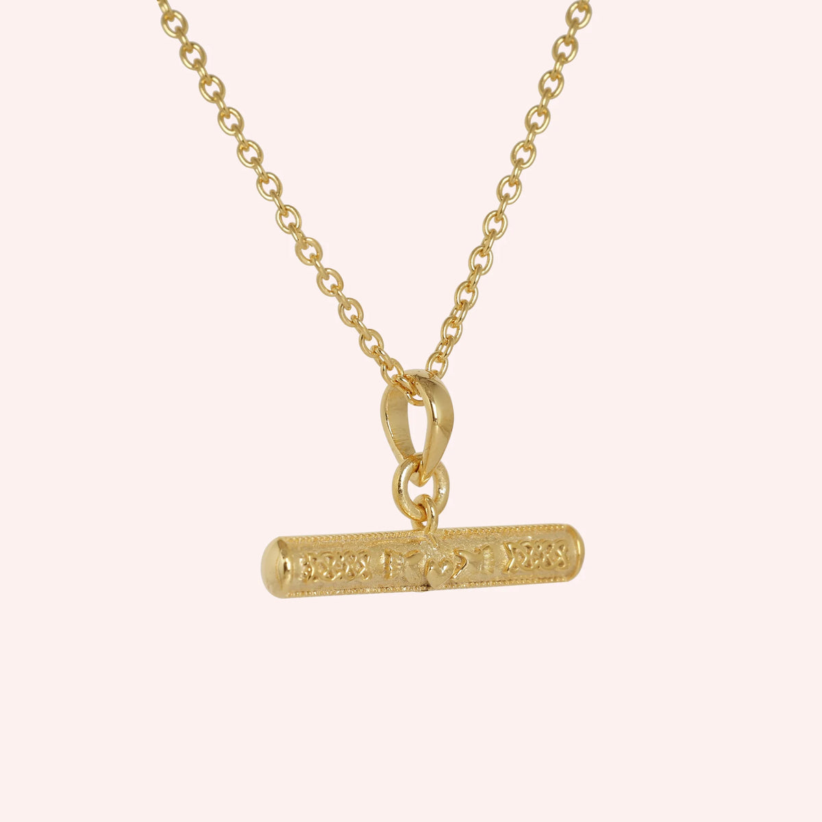 Bar_necklace_in_gold_plated_silver_with_claddagh_design_at_slight_angle_view_on_solid_pink_background