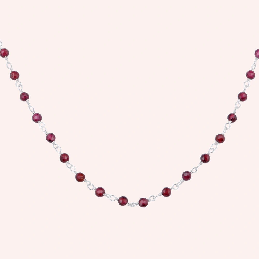 Beaded_necklace_with_sterling_silver_chain_and_deep_red_gemstone_beads_zoomed_shot_on_solid_pink_background