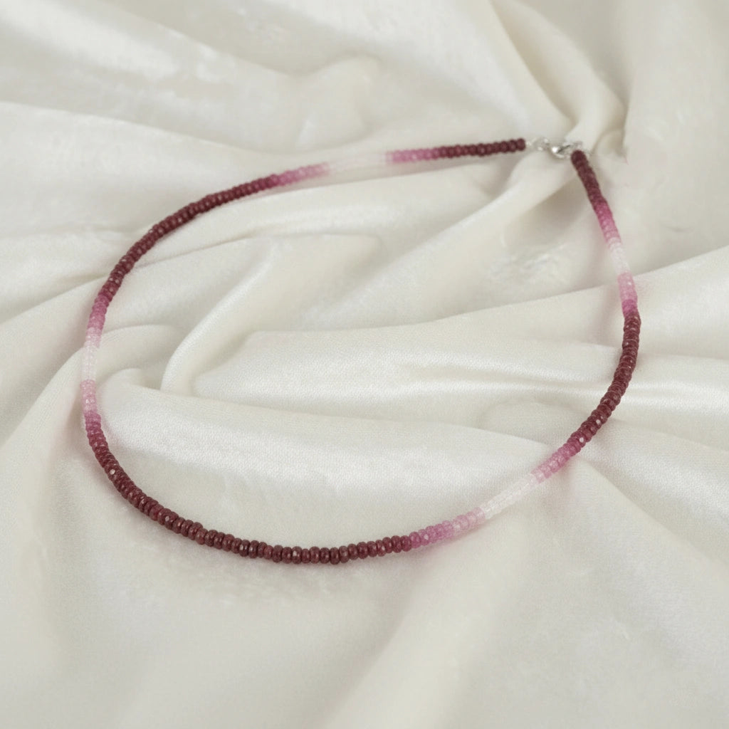 Beaded_necklace_in_ombre_effect_with_ruby_stones_in_gradient_design_in_slight_angle_on_a_white_fabric_background