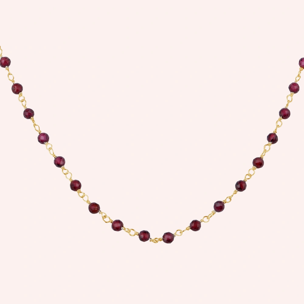 Beaded_necklace_with_gold_plated_silver_chain_and_deep_red_gemstone_beads_zoomed_shot_on_solid_pink_background
