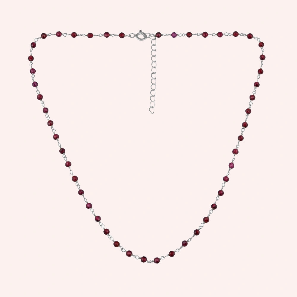 Beaded_necklace_with_sterling_silver_chain_and_deep_red_gemstone_beads_on_front_angle_view_on_slid_pink_background