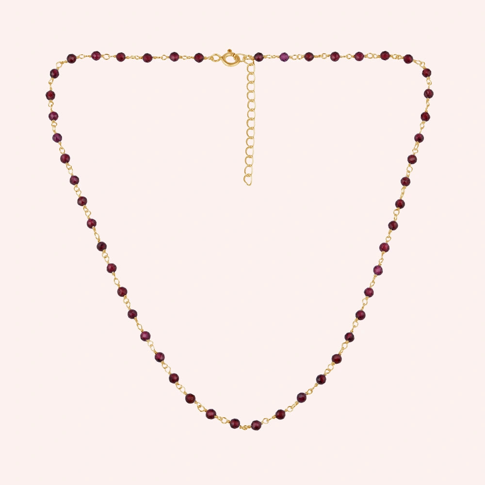 Beaded_necklace_with_gold_plated_silver_chain_and_deep_red_gemstone_beads_on_front_angle_view_on_solid_pink_background