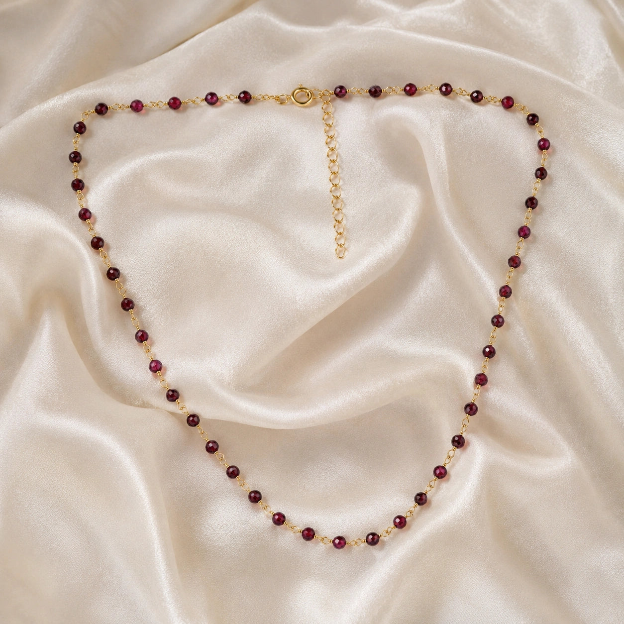 Beaded_necklace_with_gold_plated_silver_chain_and_deep_red_gemstone_beads_on_front_angle_view_on_soft_fabric_background
