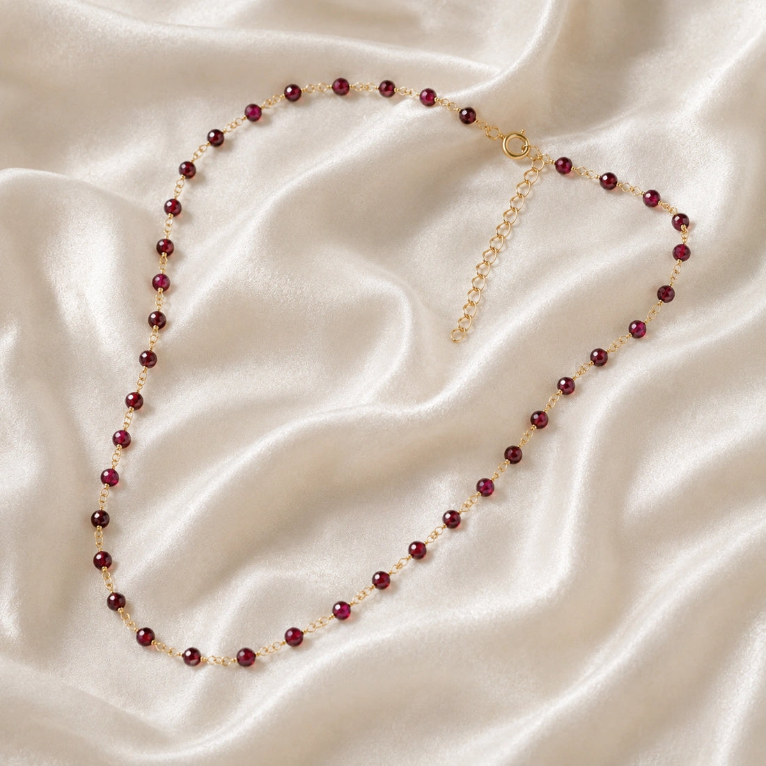 Beaded_necklace_with_gold_plated_silver_chain_and_deep_red_gemstone_beads_on_slightly_angled_view_on_soft_fabric_background