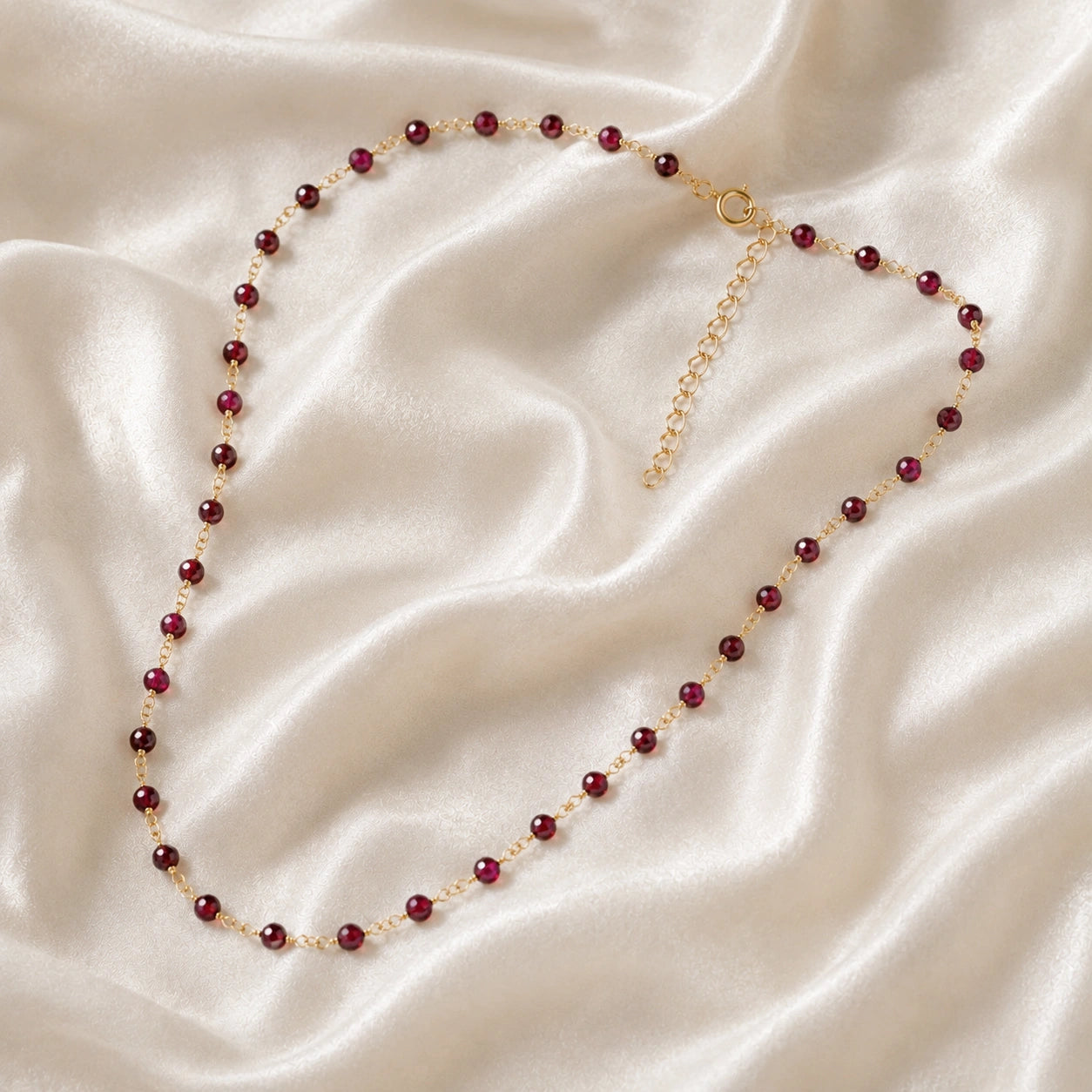 Beaded_necklace_with_gold_plated_silver_chain_and_deep_red_gemstone_beads_on_slightly_angled_view_on_soft_fabric_background