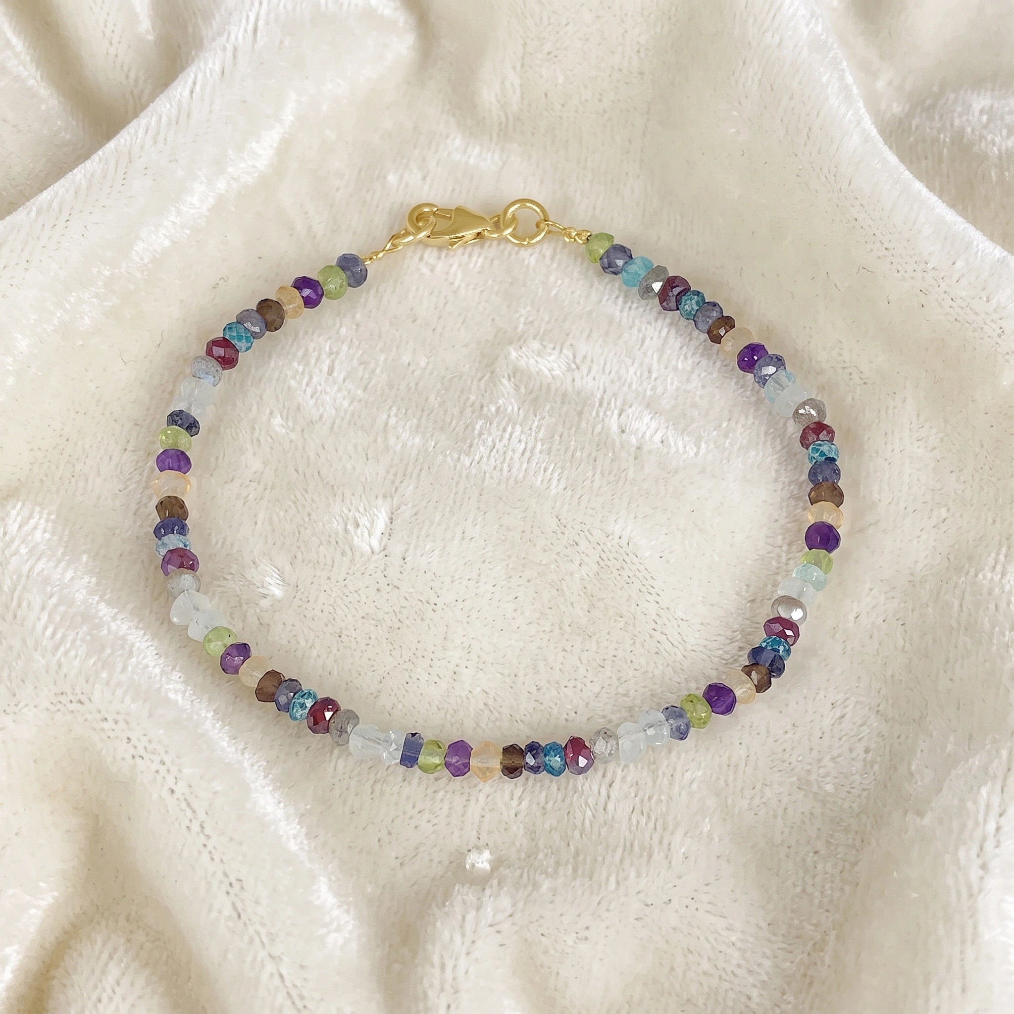 Beads_bracelet_with_multi_stones_in_gold_plated_silver_at_front_angle_view_on_soft_fabric_background