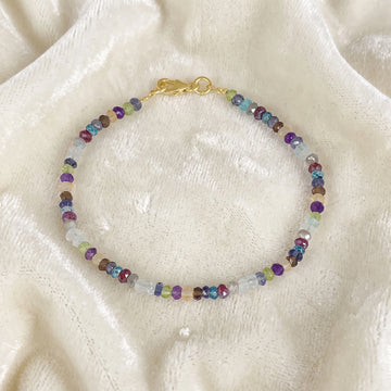 Beads_bracelet_with_multi_stones_in_gold_plated_silver_at_front_angle_view_on_soft_fabric_background