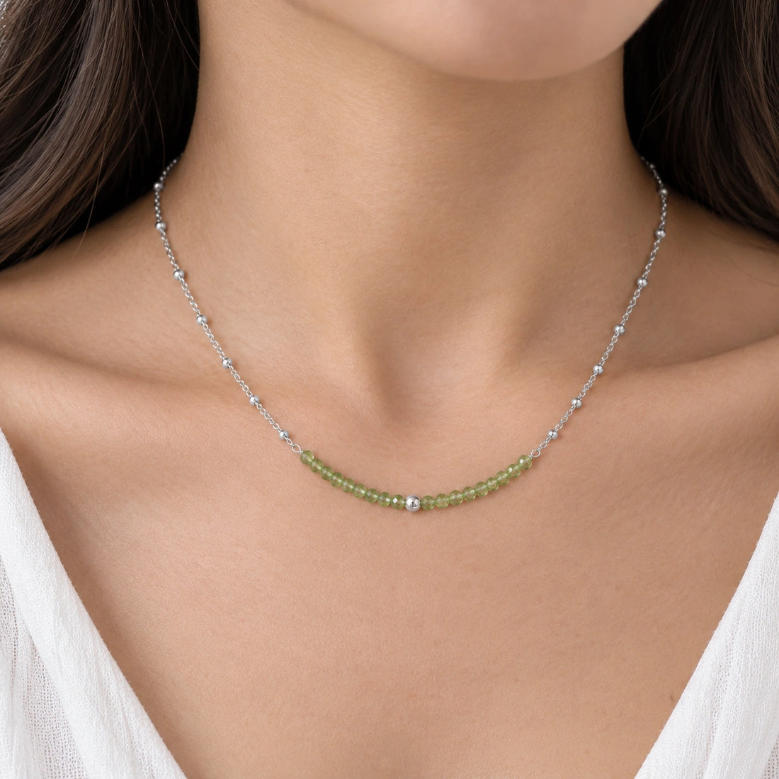 Peridot_necklace_in_sterling_silver_with_peridot_stones_in_beaded_design_in_zoomed_view_on_a_white_fabric_background